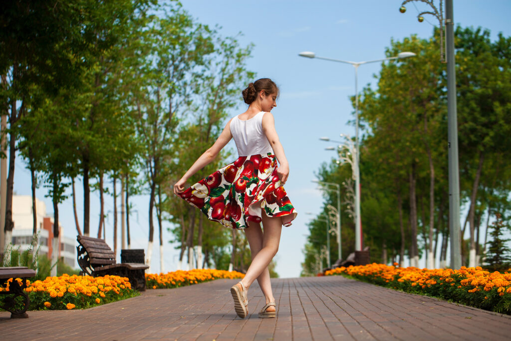 Full body portrait of a young brunette woman walking in flowers dress, summer park outdoors
